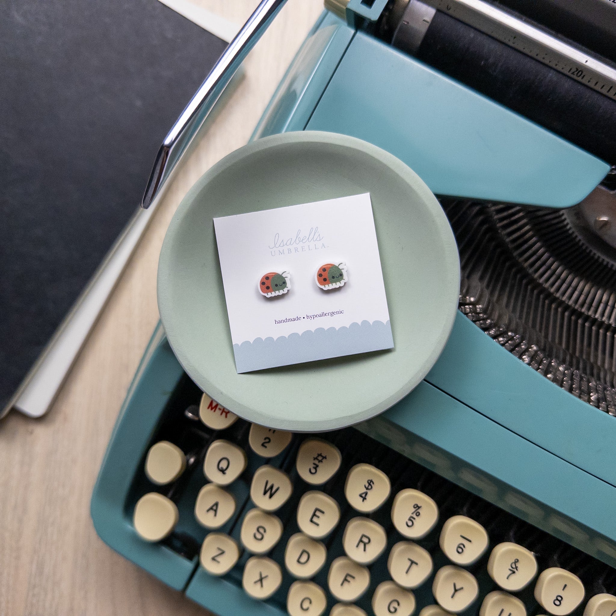 pair of adorable ladybug earrings sitting in green circular tray set on top of a teal vintage typewriter.