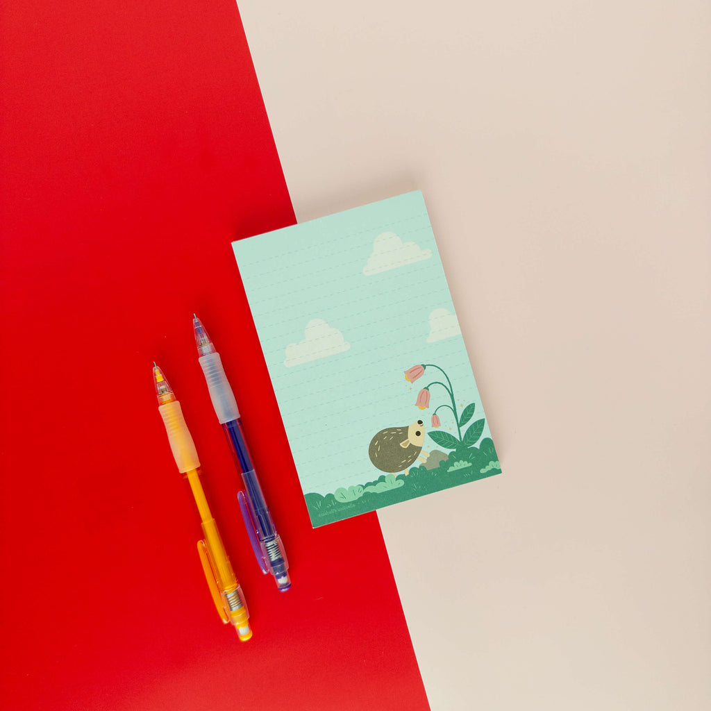 Hedgehog illustrated notepad displayed on a red and cream background with colorful pens.