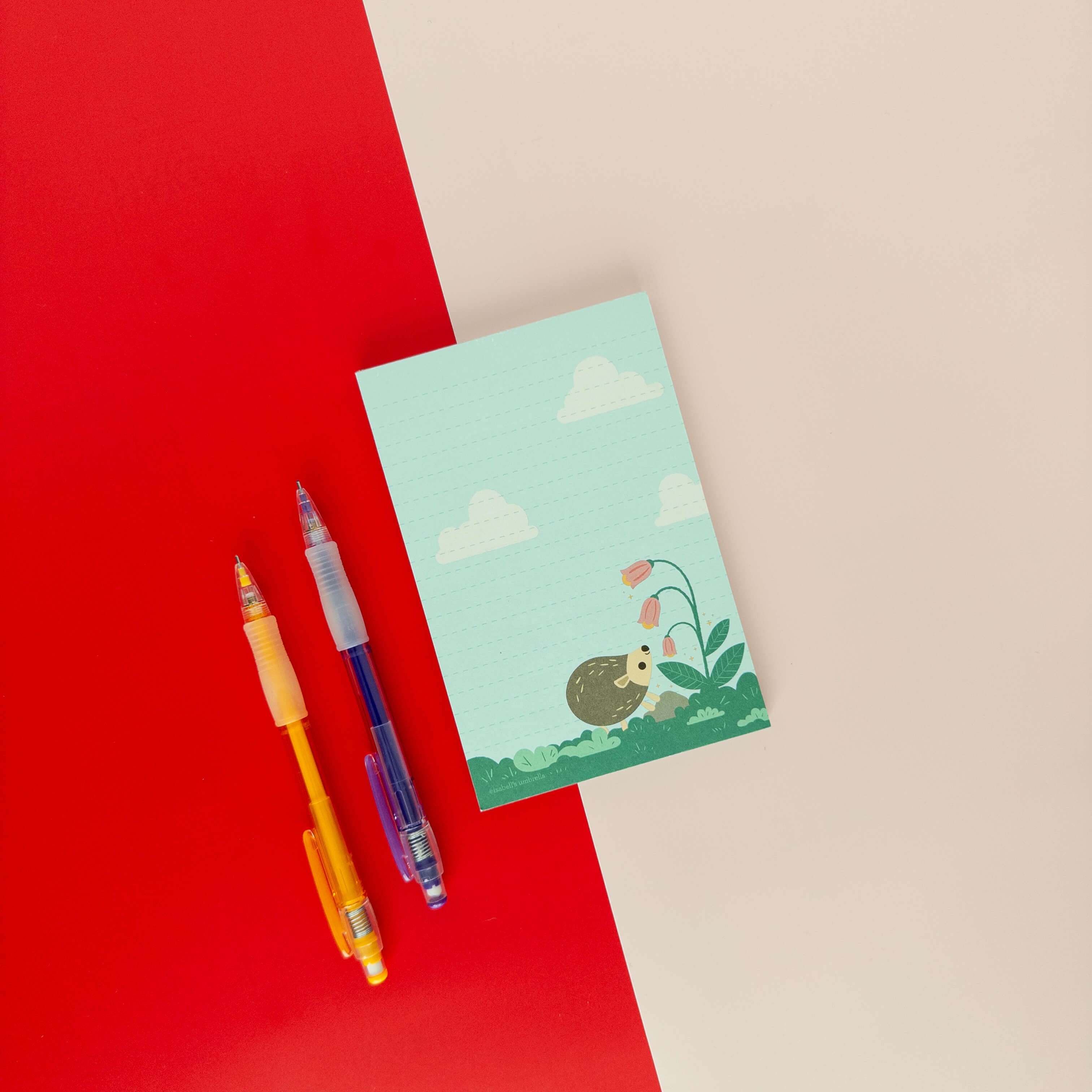 Hedgehog illustrated notepad displayed on a red and cream background with colorful pens.