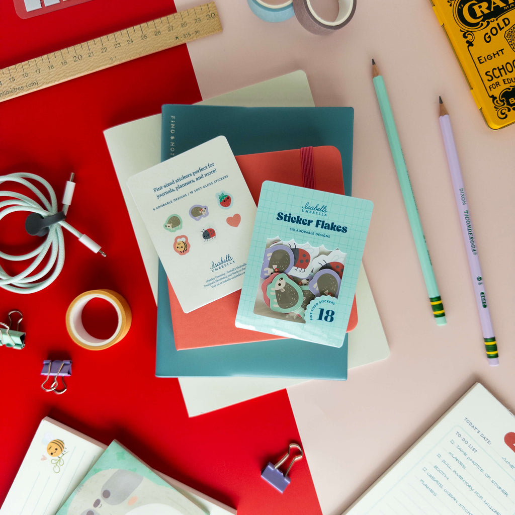Hedgehog sticker flakes displayed with their packaging and individual stickers on a colorful desk.