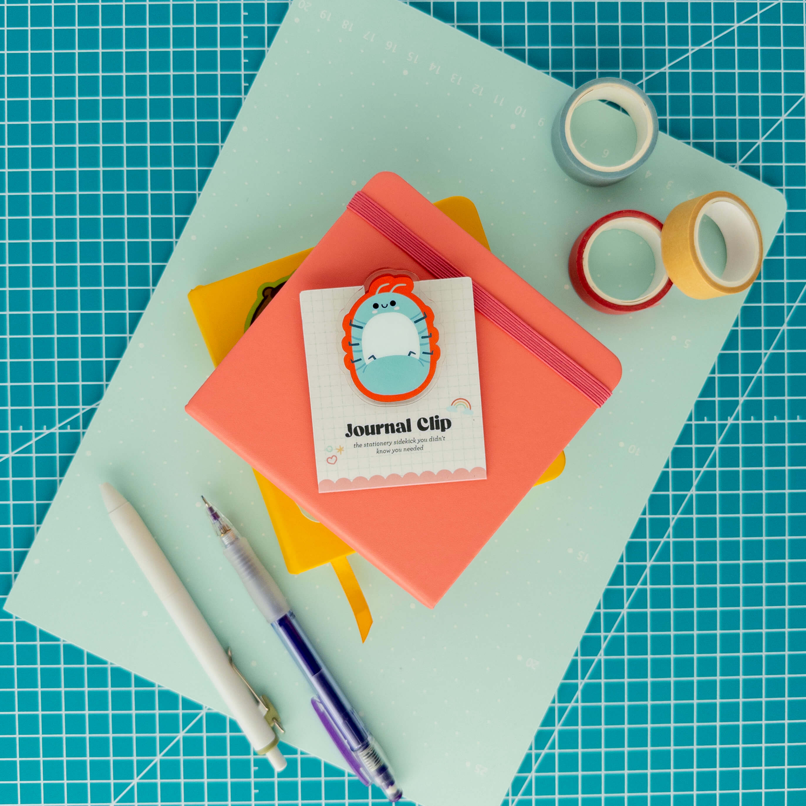 Cute roly poly acrylic journal clip displayed on its backing card with colorful paper, washi tape, and pens.
