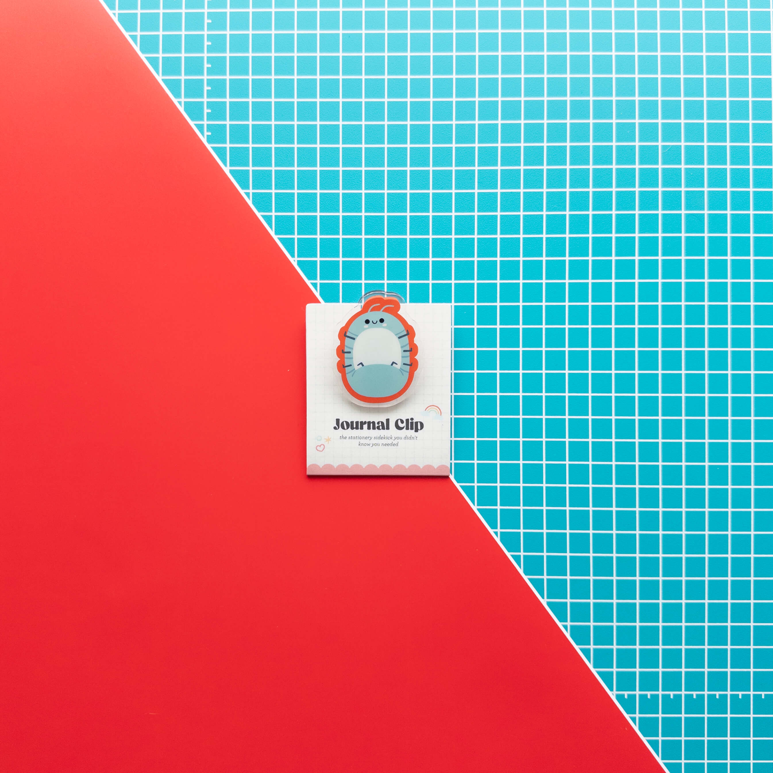 Cute roly poly acrylic journal clip displayed on its branded backing card against a colorful red and grid background.