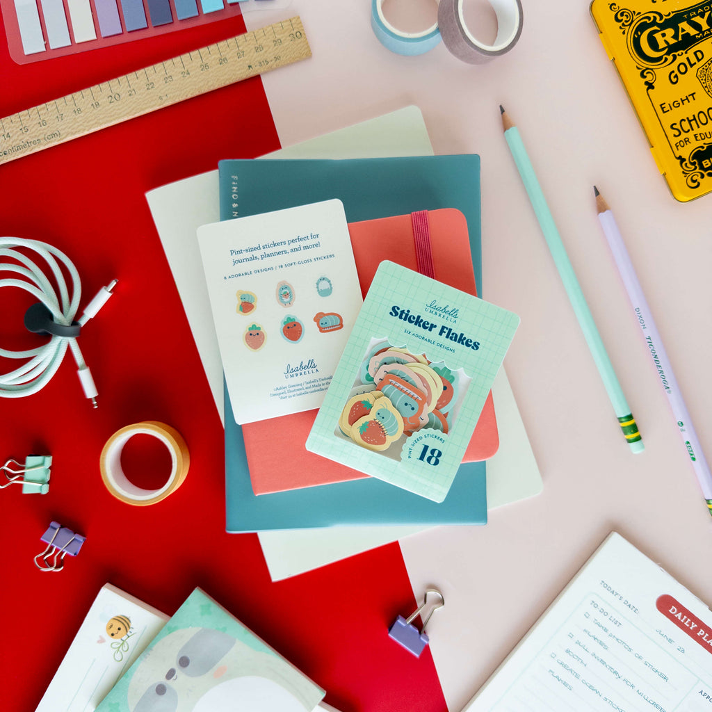 Roly poly sticker flakes displayed with their packaging and individual stickers on a colorful desk.