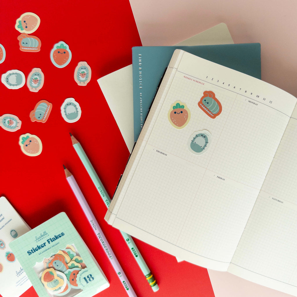 Cute roly poly stickers decorating an open grid notebook surrounded by colorful stationery.