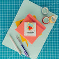 Cute roly poly on a strawberry acrylic journal clip displayed on its backing card with colorful paper, washi tape, and pens.