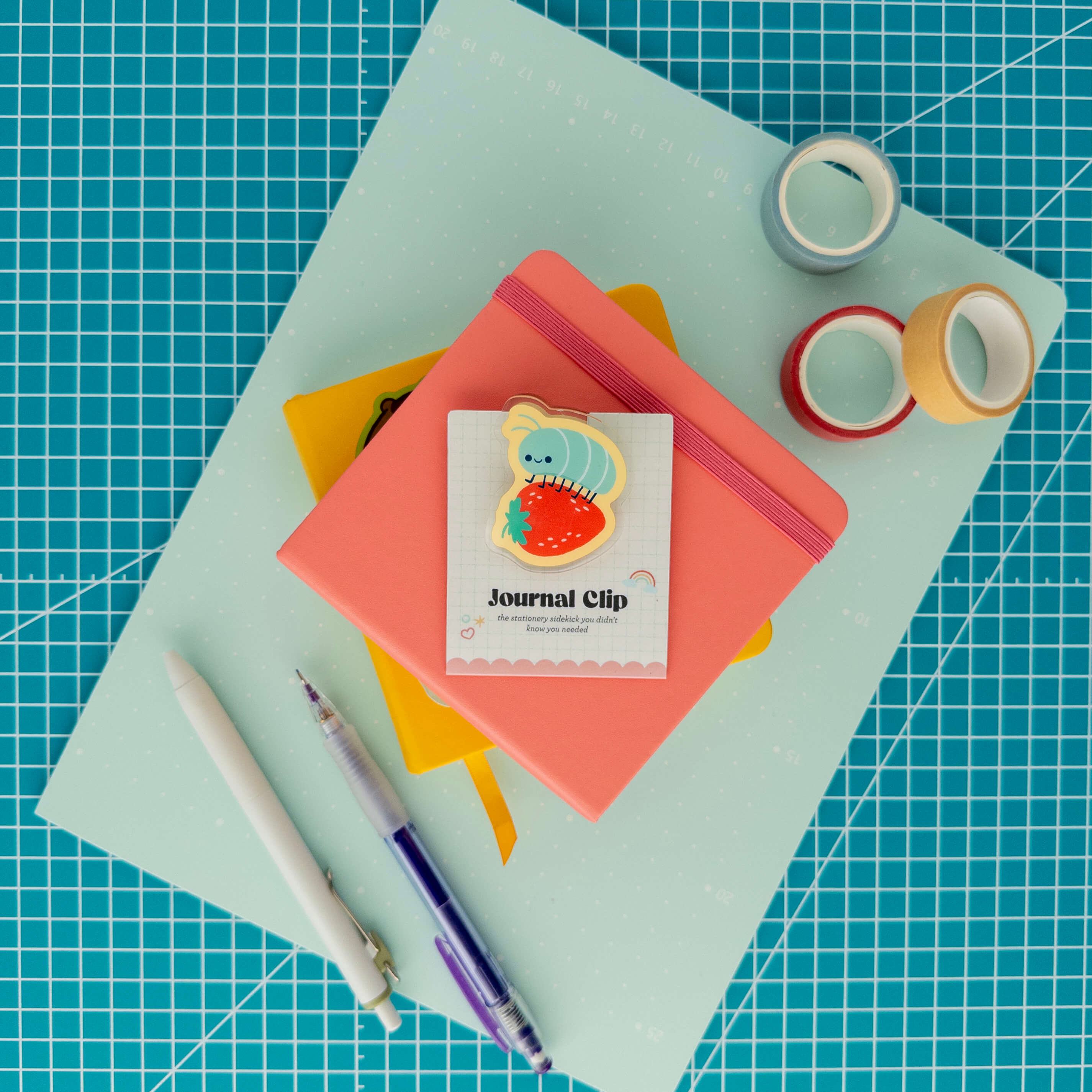 Cute roly poly on a strawberry acrylic journal clip displayed on its backing card with colorful paper, washi tape, and pens.