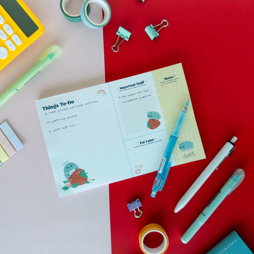 Cute roly poly planner notepad displayed on a red and cream background with pens and stationery.