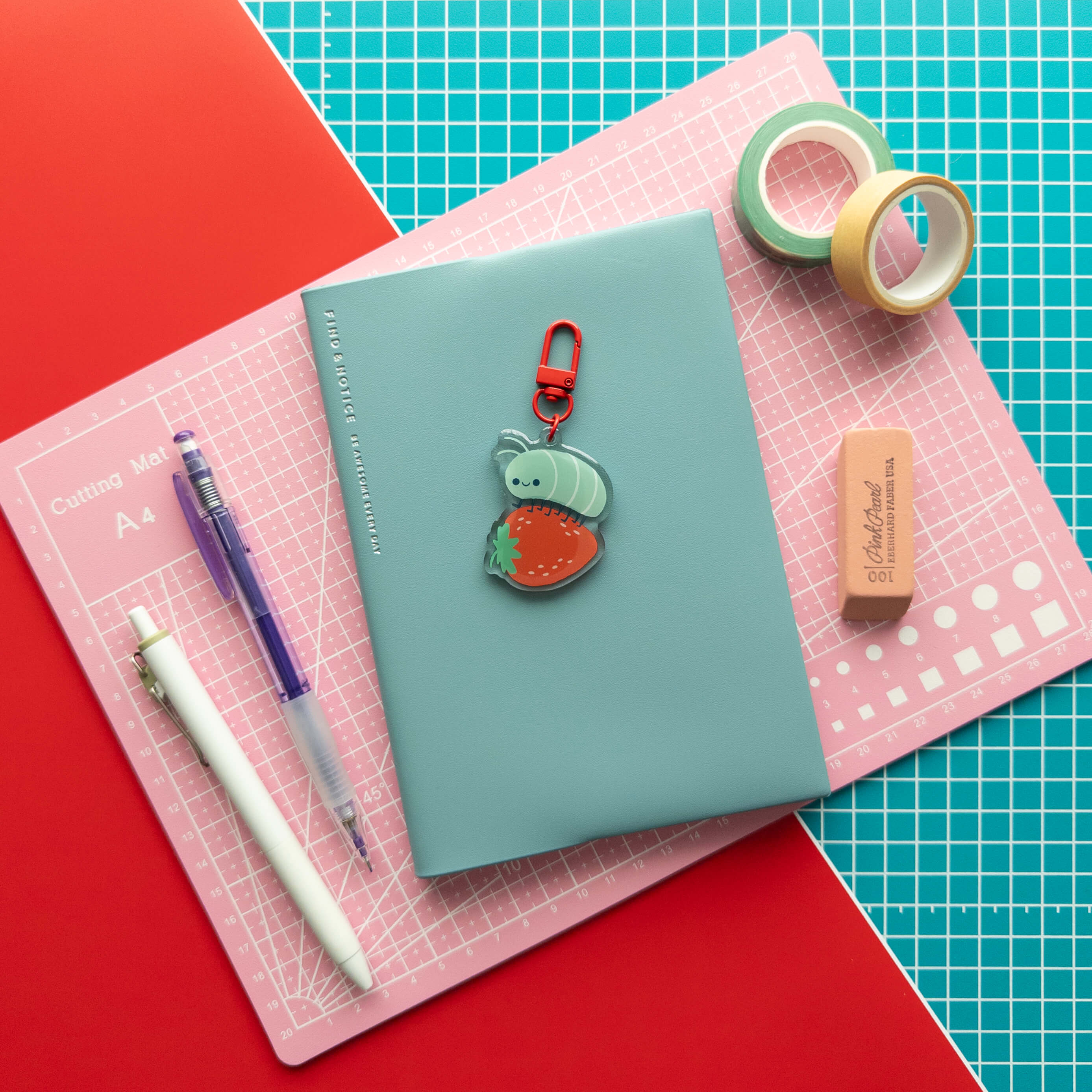 Cute roly poly on a strawberry acrylic keychain displayed on a teal notebook with colorful stationery.