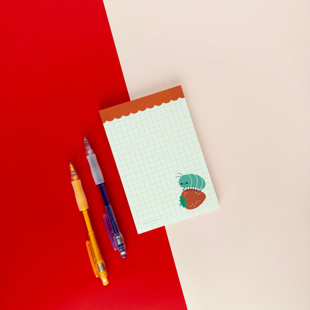 Roly poly on a strawberry illustrated notepad displayed on a red and cream background with colorful pens.