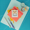 Cute sloth acrylic journal clip displayed on its backing card with colorful paper, washi tape, and pens.