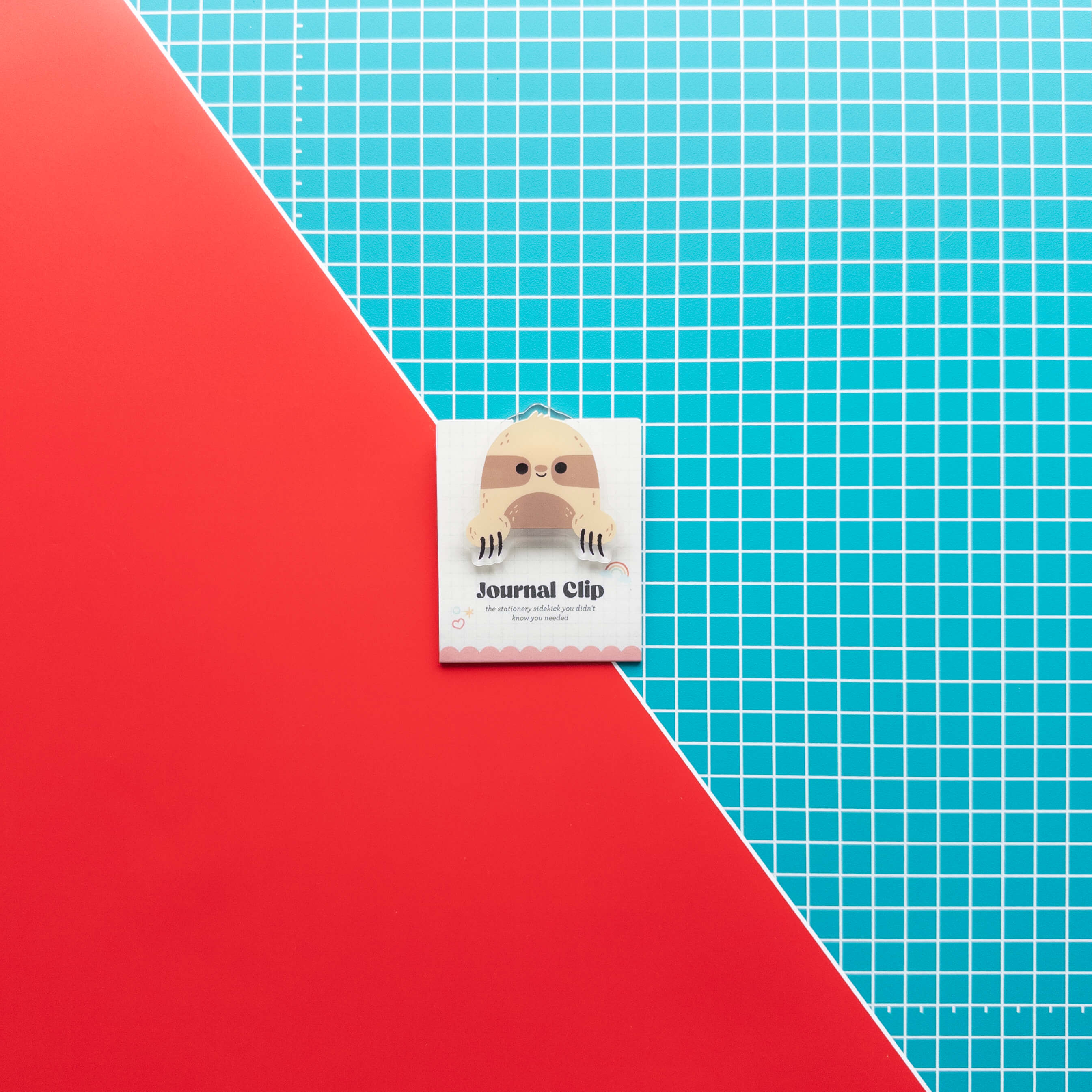 Cute sloth acrylic journal clip displayed on its branded backing card against a colorful red and grid background.