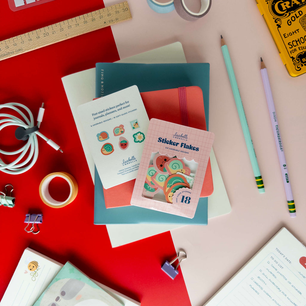 Snail sticker flakes displayed with their packaging and individual stickers on a colorful desk.