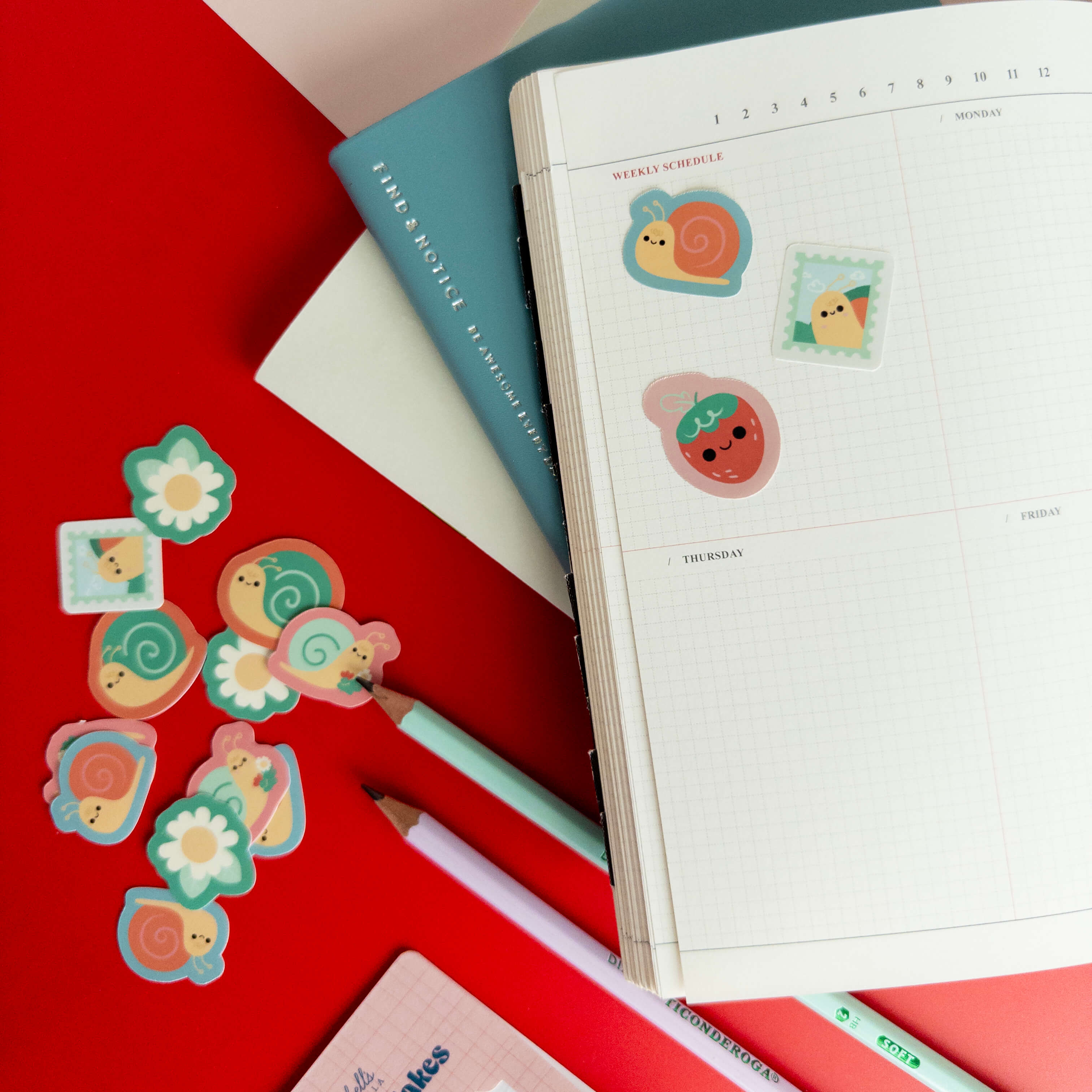 Cute snail sticker flakes scattered around an open grid notebook and colorful stationery.