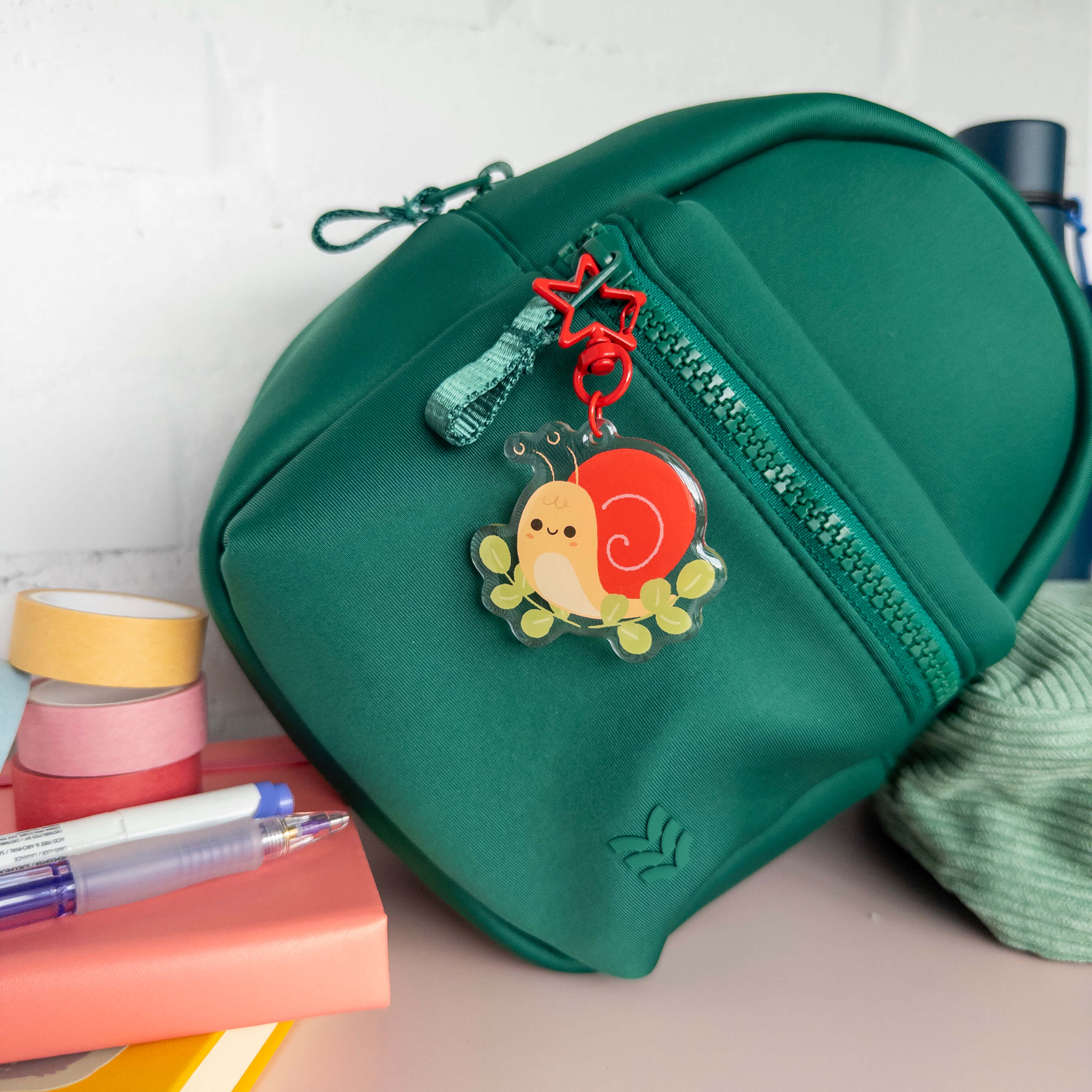 Small green backpack with a snail charm keychain on a white background