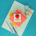 Cute strawberry acrylic journal clip displayed on its backing card with colorful paper, washi tape, and pens.