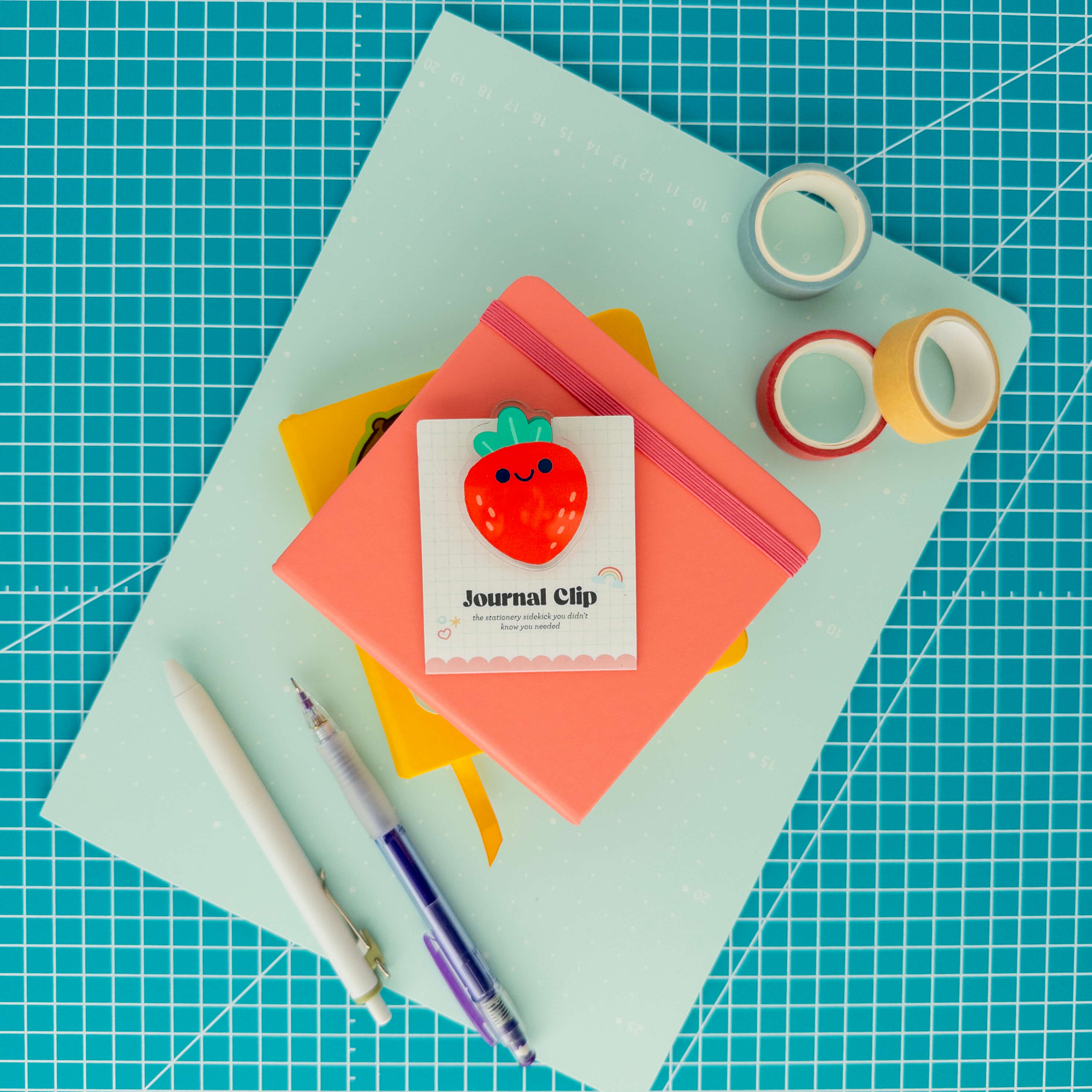 Cute strawberry acrylic journal clip displayed on its backing card with colorful paper, washi tape, and pens.