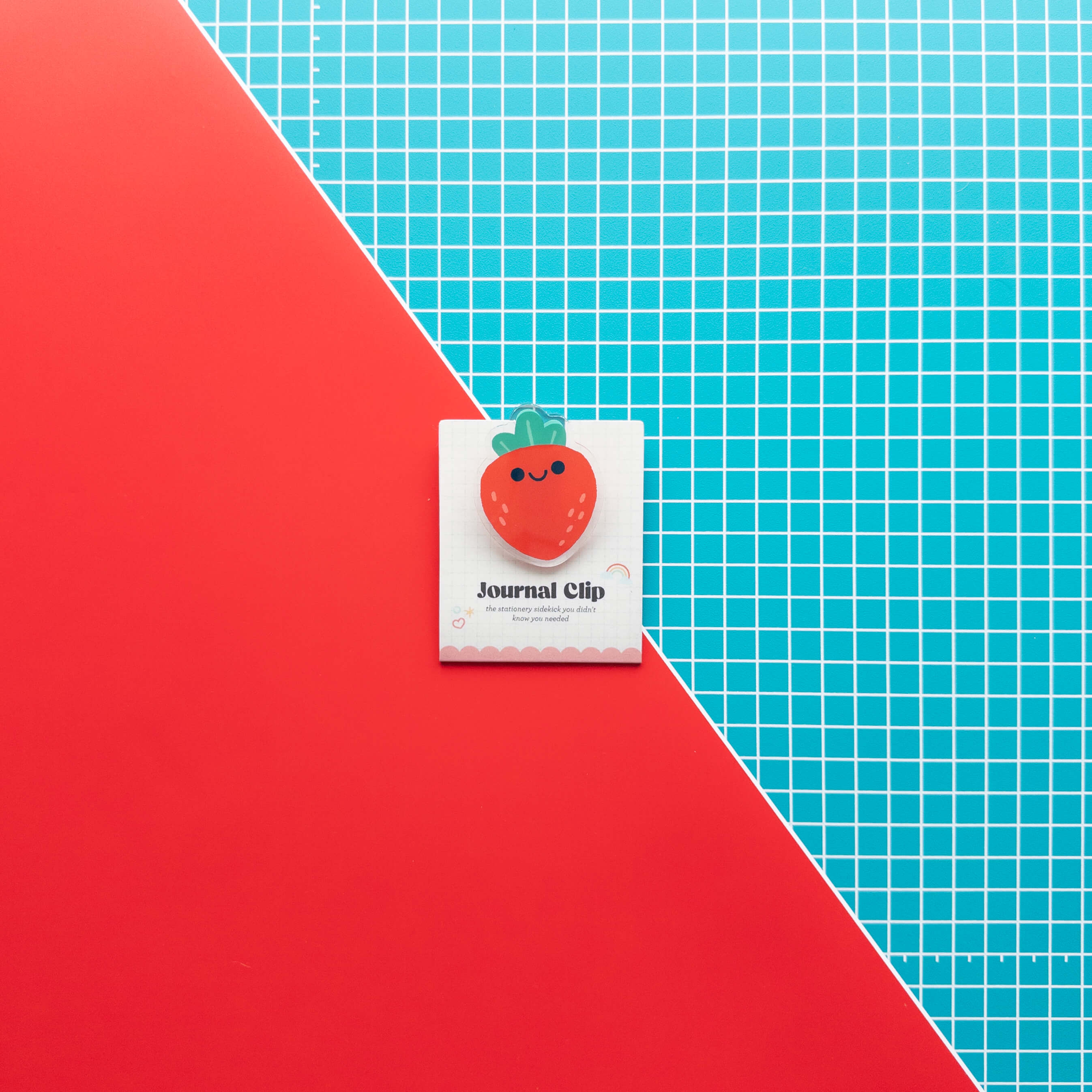 Cute strawberry acrylic journal clip displayed on its branded backing card against a colorful red and grid background.
