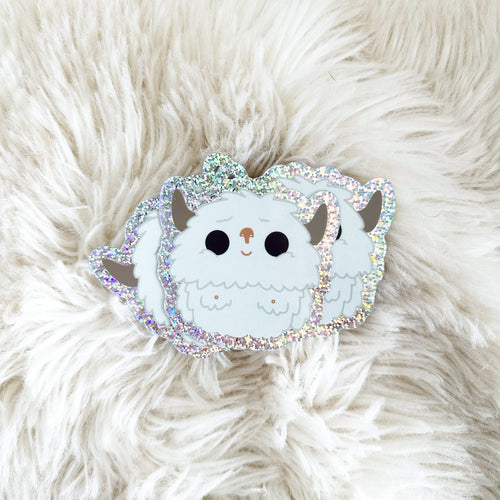 A cute glittery yeti vinyl sticker sitting on a faux sheep skin blanket