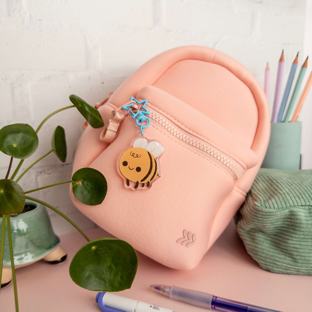 Pink backpack with bee charm keychain on a desk with stationery items