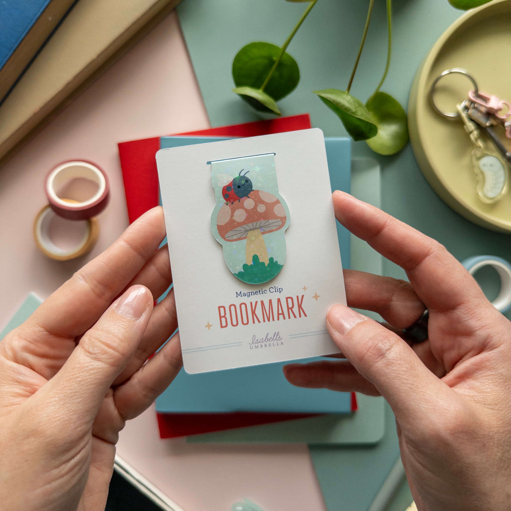 Mushroom-shaped magnetic clip bookmark held by hands with a colorful background