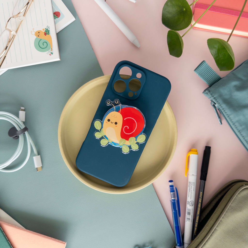 Phone case with a snail designed magnetic phone grip on a table with stationery items