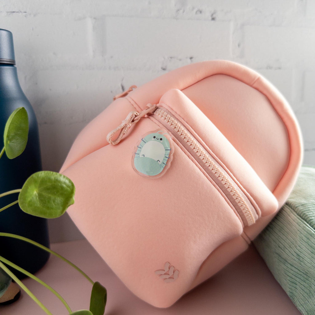Cute Roly Poly acrylic pin with glossy epoxy finish, attached to a pink backpack pictured with a plant and blue water bottle.
