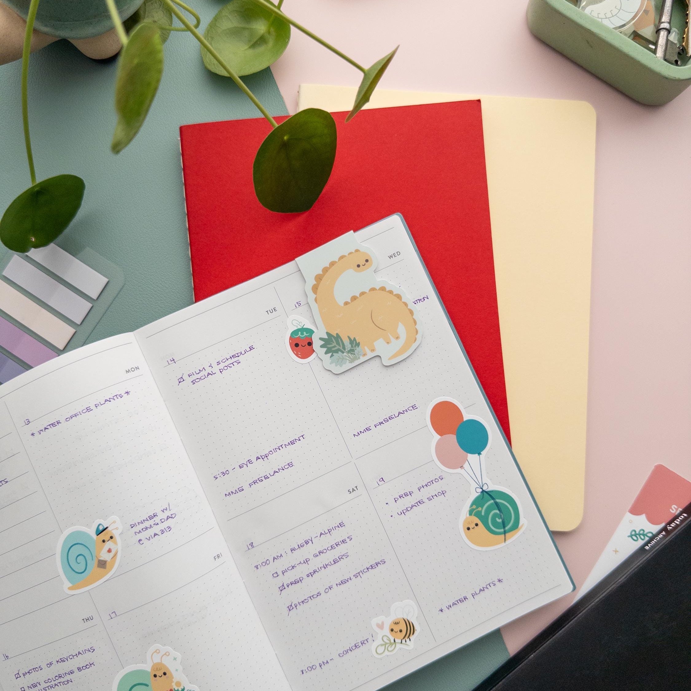 Brontosaurus magnetic bookmark holding a page in an open book, adorable dinosaur reading accessory for students and book lovers.