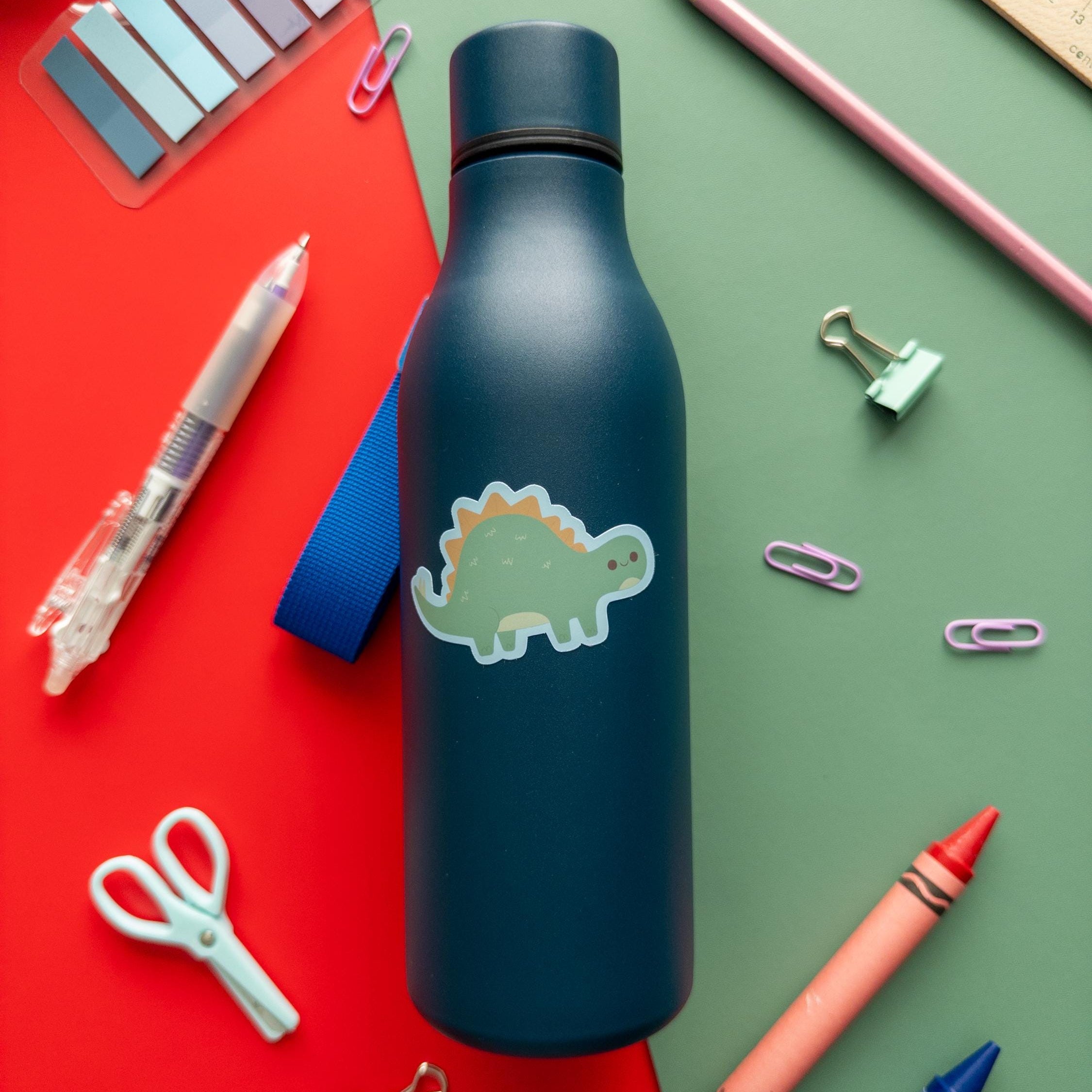 Blue water bottle with dinosaur design on a colorful background with stationery items