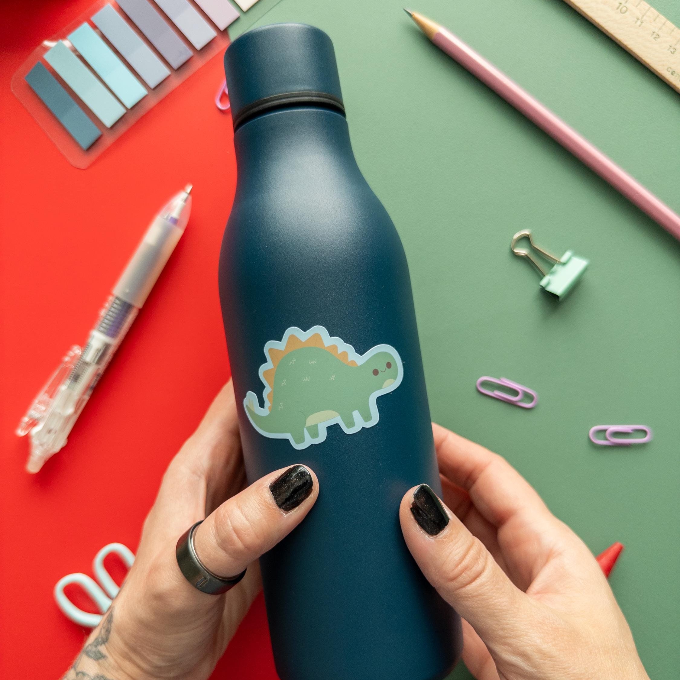 Person holding a blue water bottle with a dinosaur design on a colorful background