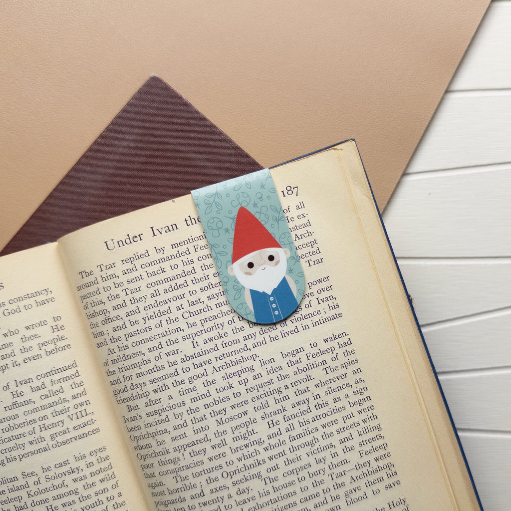 Magnetic bookmark of an illustrated gnome clipped to a page of a book.