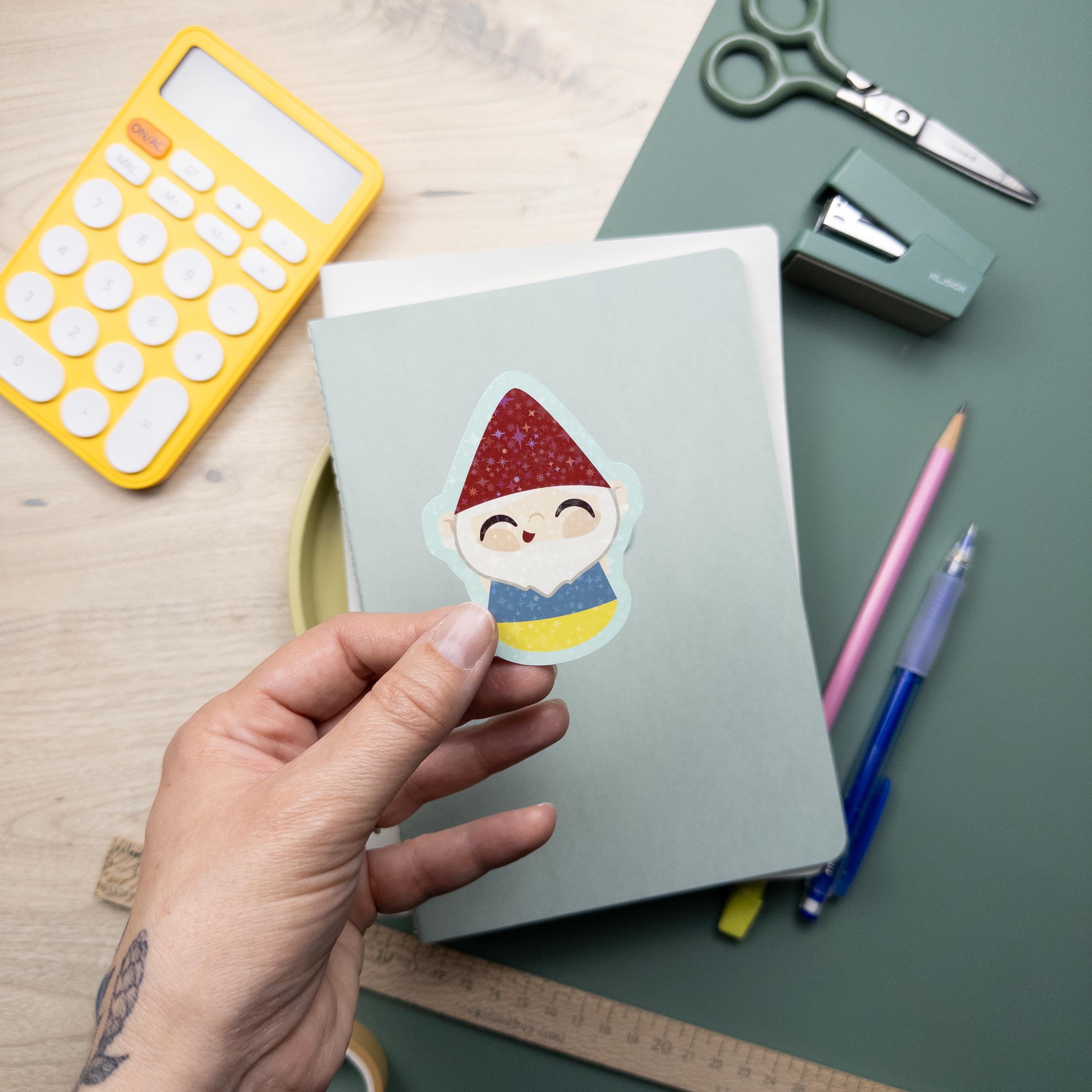 Hand holding a cute glitter garden gnome vinyl sticker, waterproof and durable kawaii decal for laptops, water bottles, and journals, cottagecore design.
