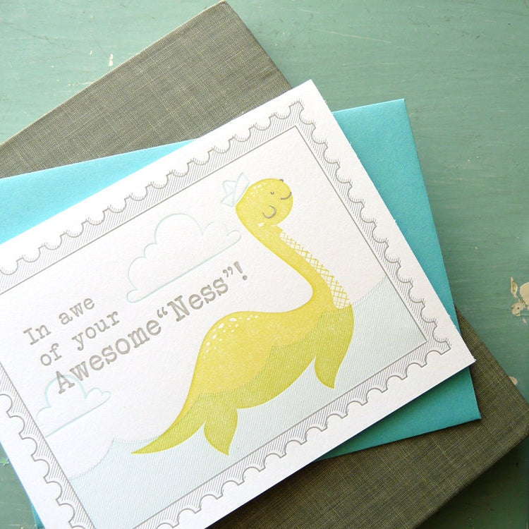 Card with a Loch Ness Monster illustration and on a green surface with a pencil.