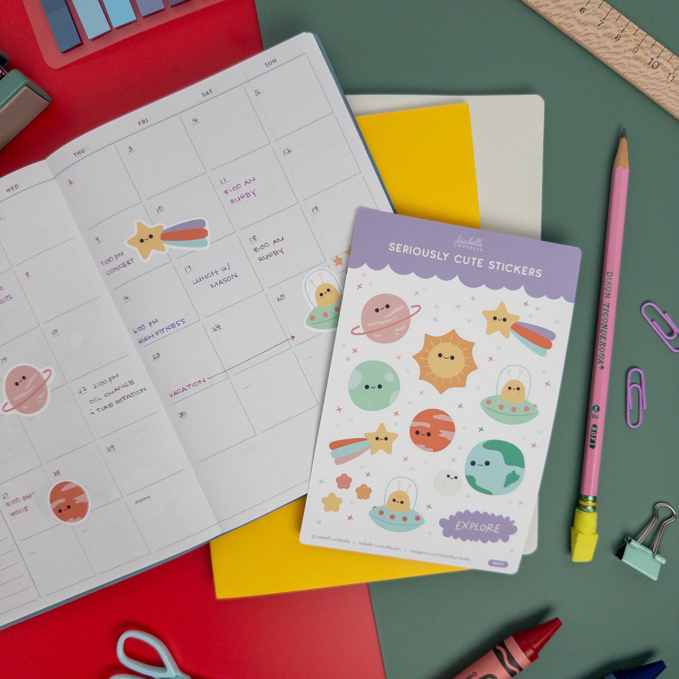Kawaii planet sticker sheet next to an open planner with stickers applied, surrounded by school and art supplies on a red and green background.