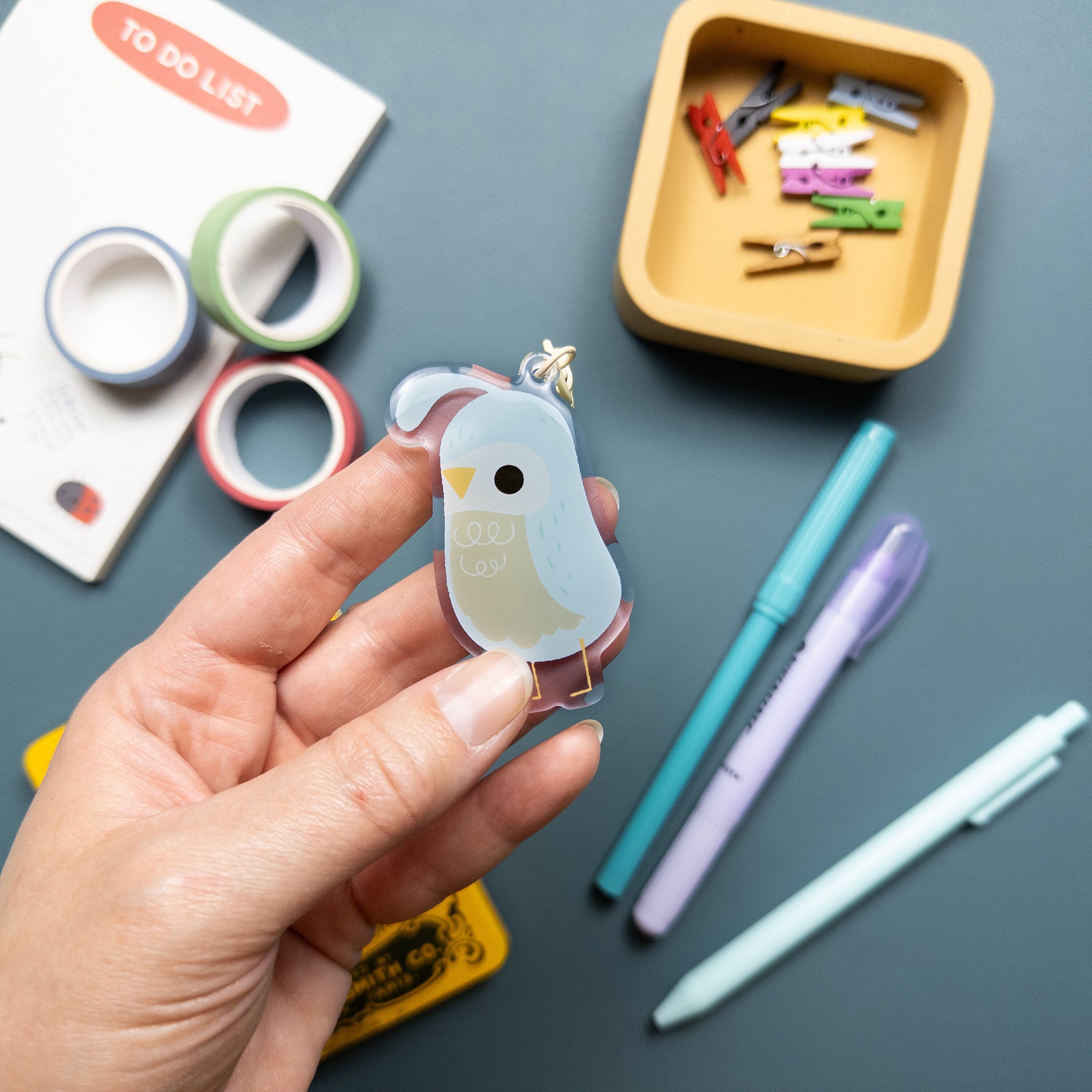 Hand holding an acrylic keychain featuring an illustrated quail