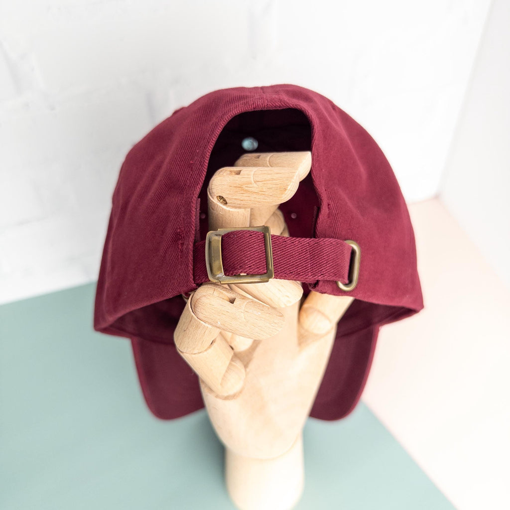Maroon cap with a strap held by a hand on a light green surface.