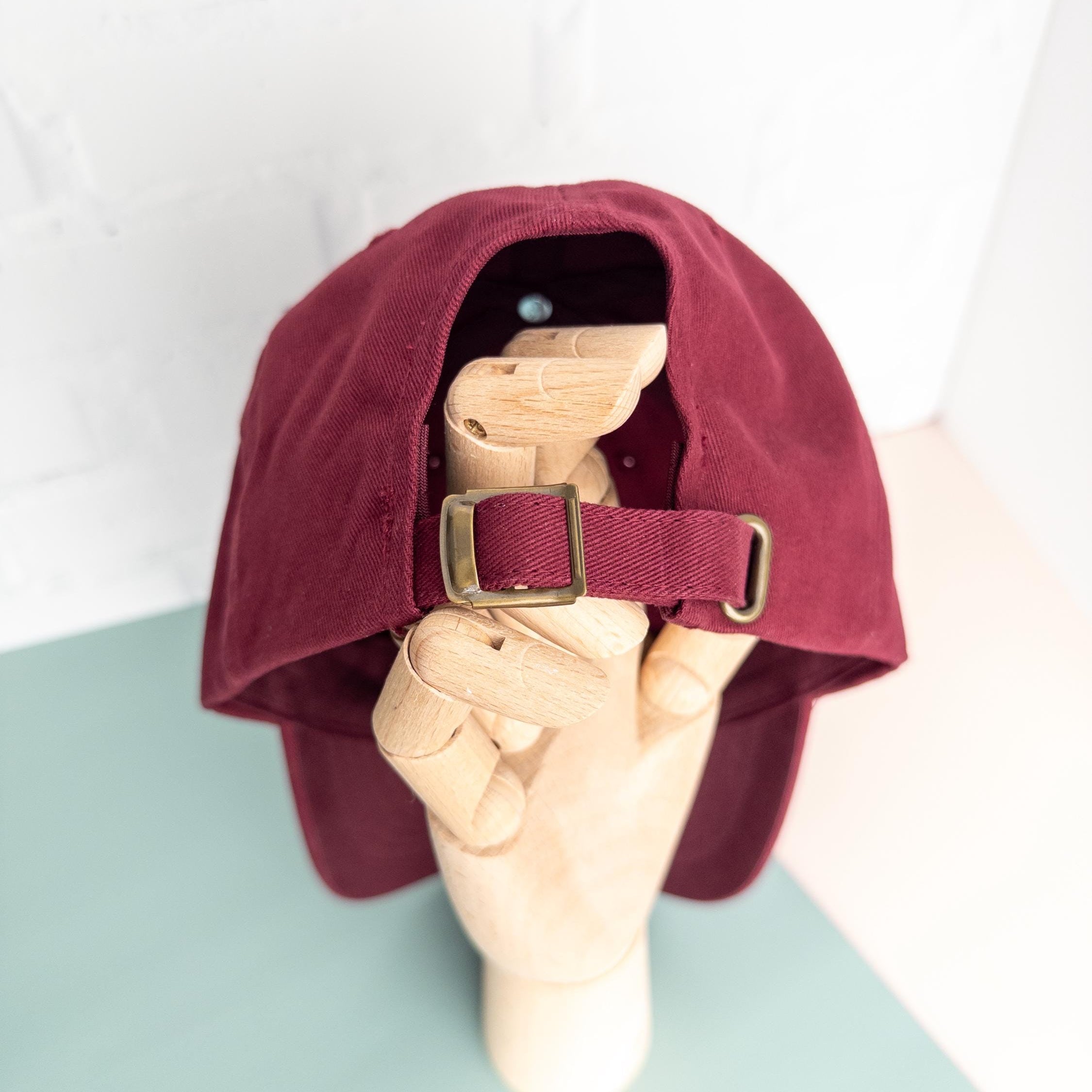 Maroon cap with a strap held by a hand on a light green surface.