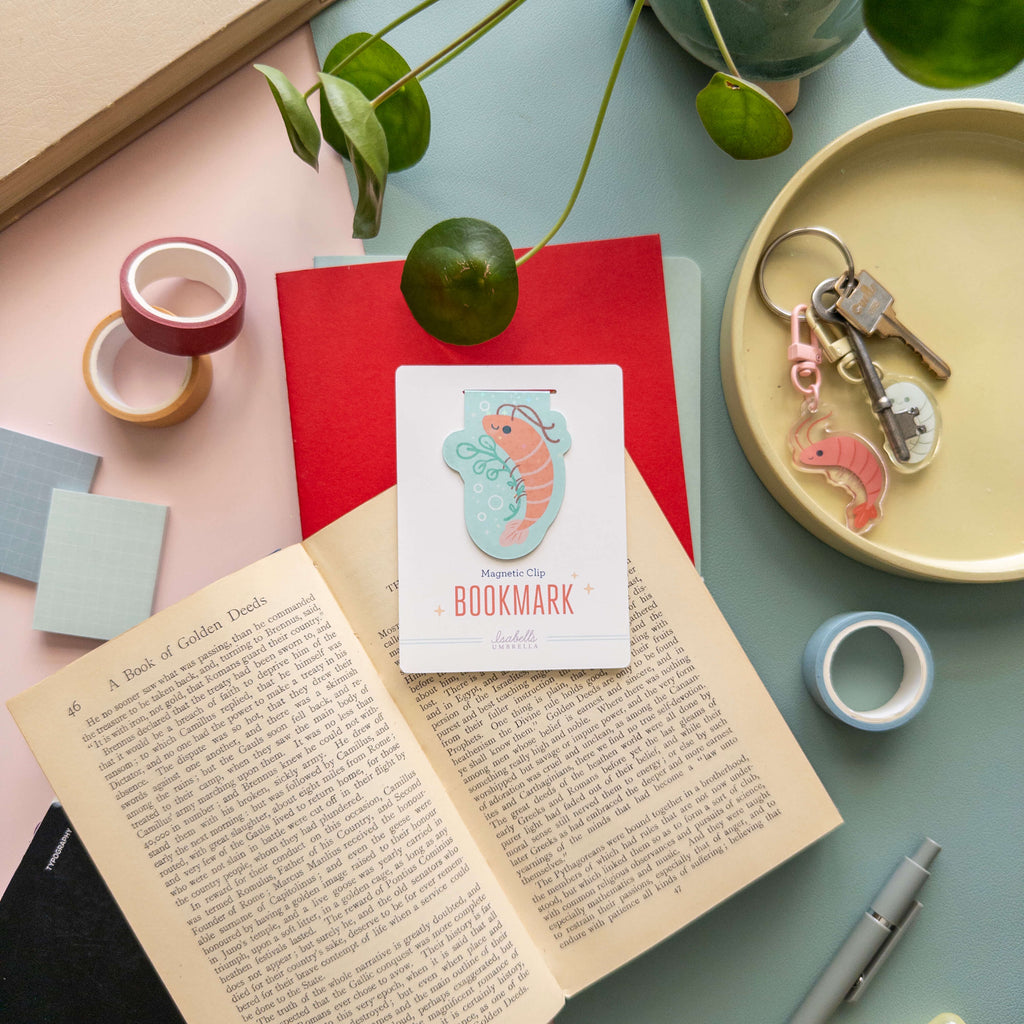 Shrimp-themed bookmark on an open book with stationery items on a table.