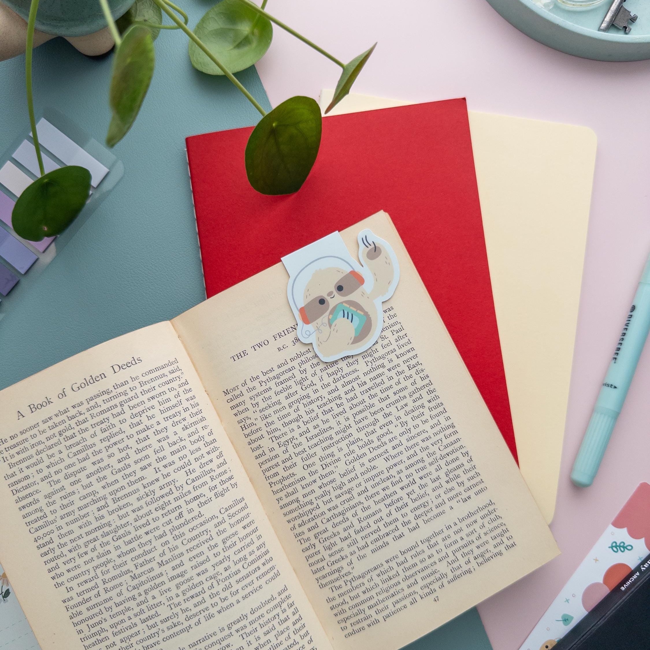 Sloth with Walkman magnetic bookmark clipped on an open book page, cute retro reading accessory for cozy readers and students.
