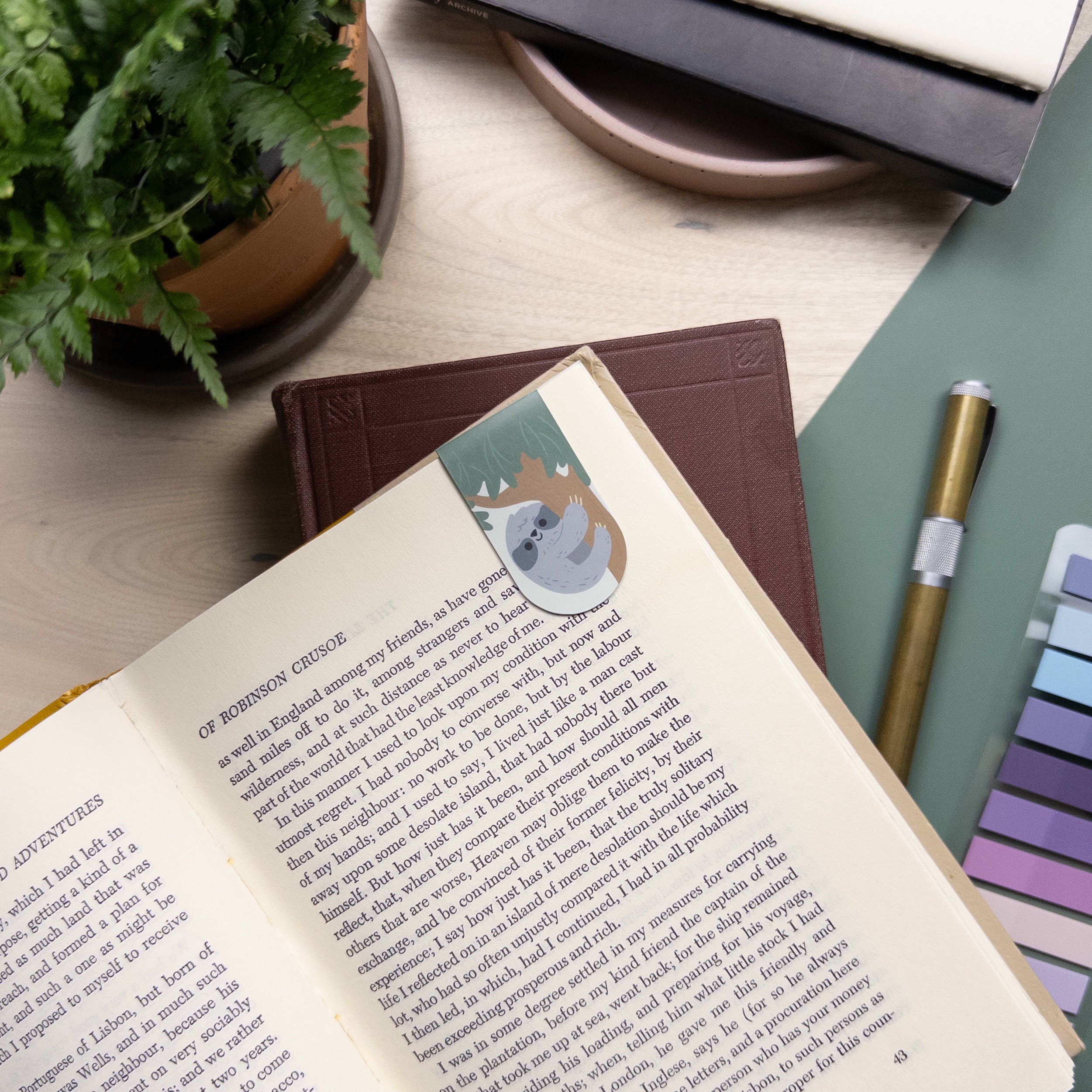 Cute illustrated sloth magnetic bookmark clipped on a book page, laminated for durability, perfect for journals, planners, and readers.