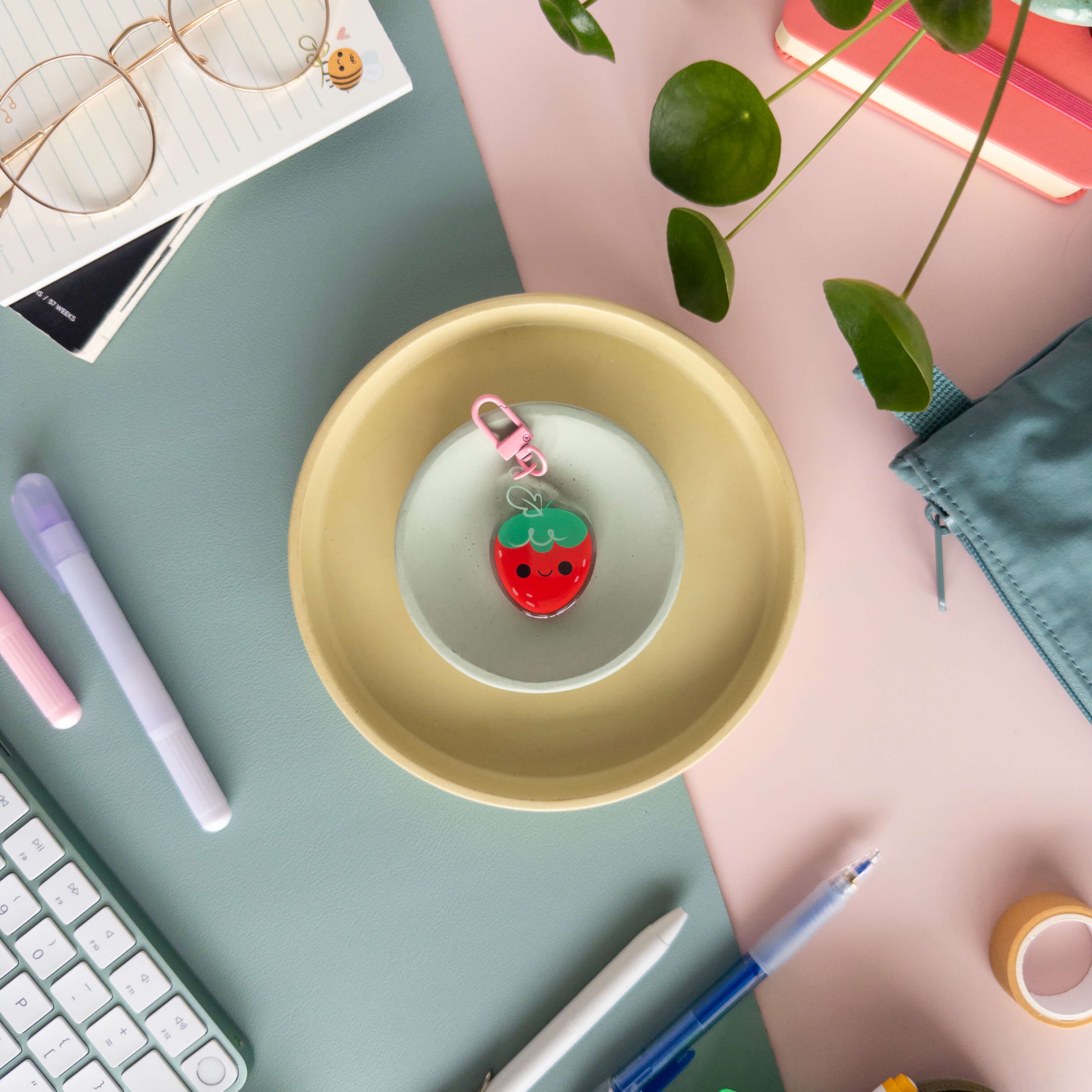 Yellow dish with strawberry-shaped keychain on a desk with stationery items