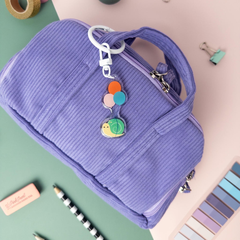 Snail and balloon acrylic keychain attached to a purple textured bag