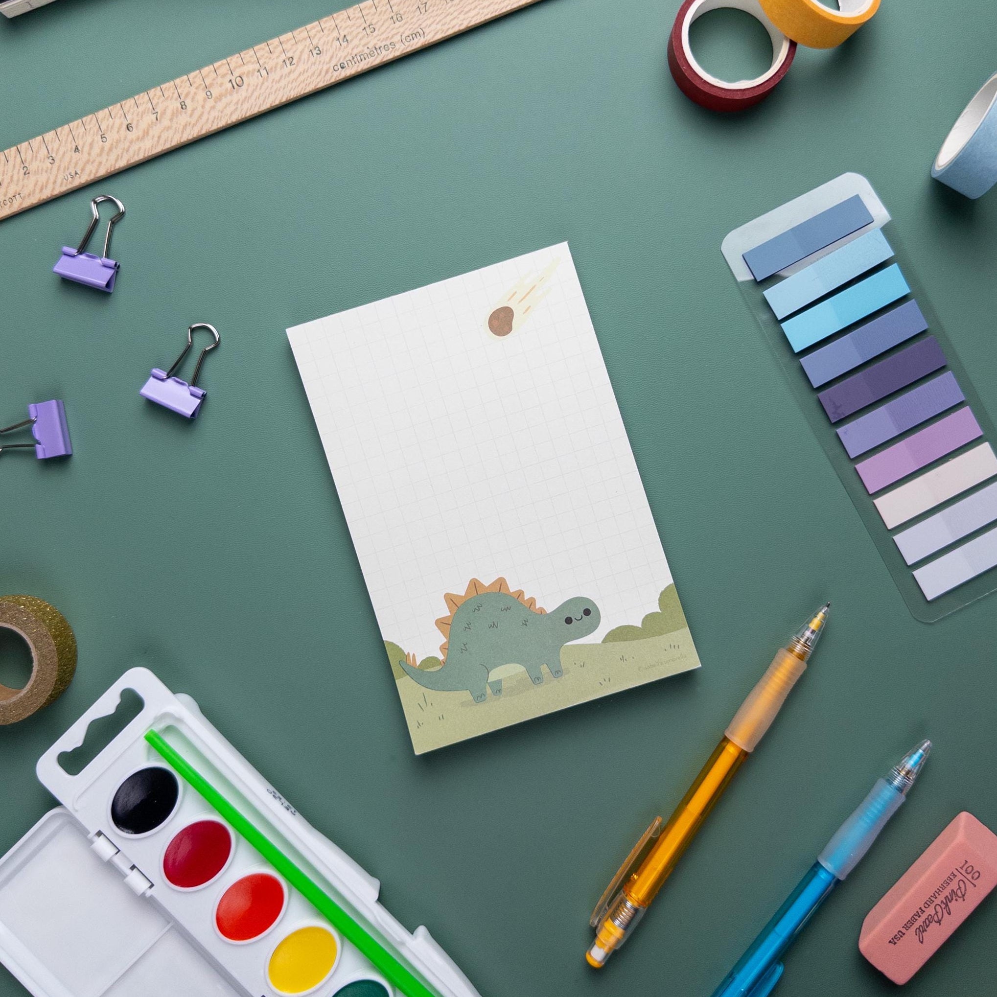 Kawaii stegosaurus dinosaur notepad with grid paper, 50 tear-off sheets, and sturdy chipboard backing, perfect for kids and stationery lovers.