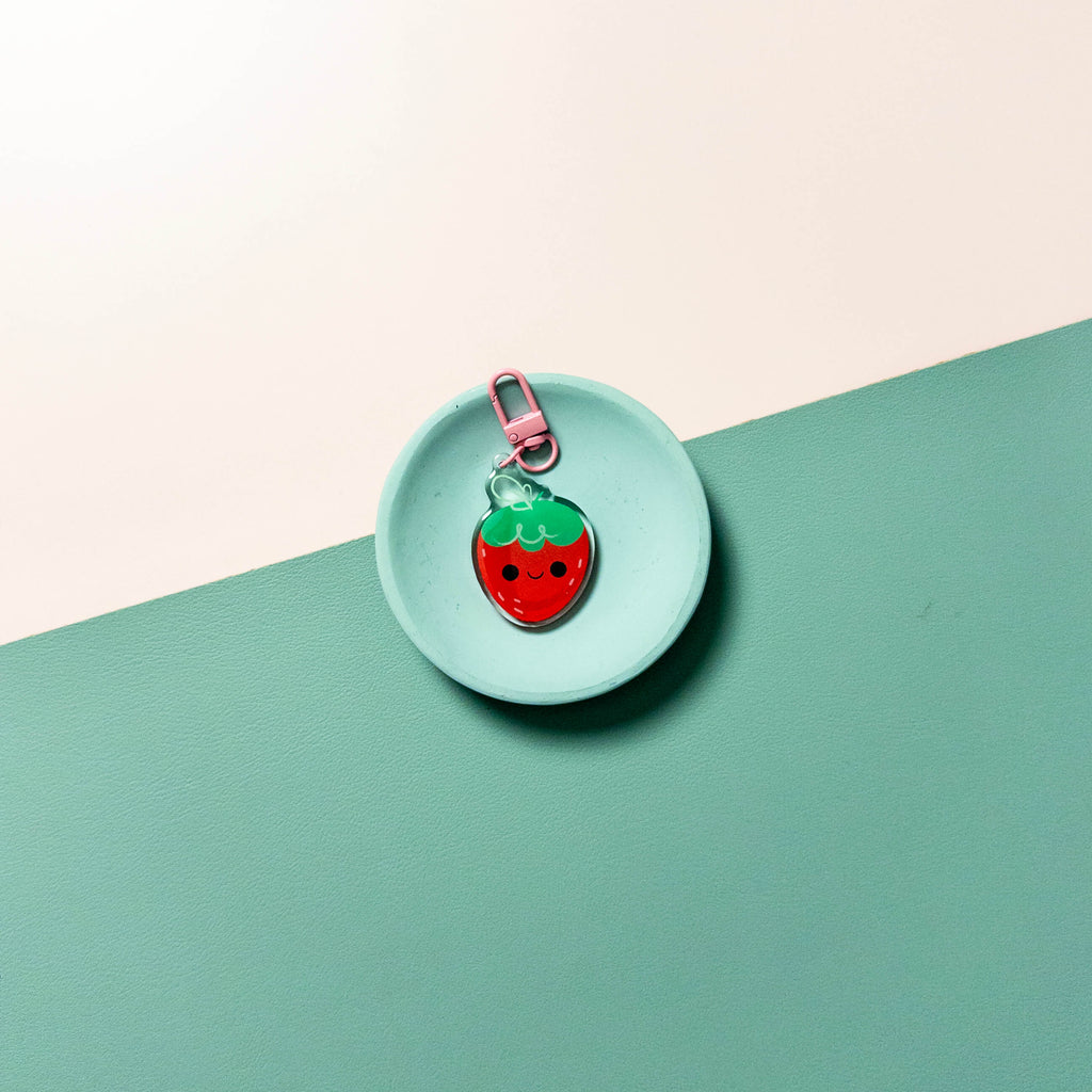 Strawberry-shaped keychain on a round turquoise tray with a light pink background