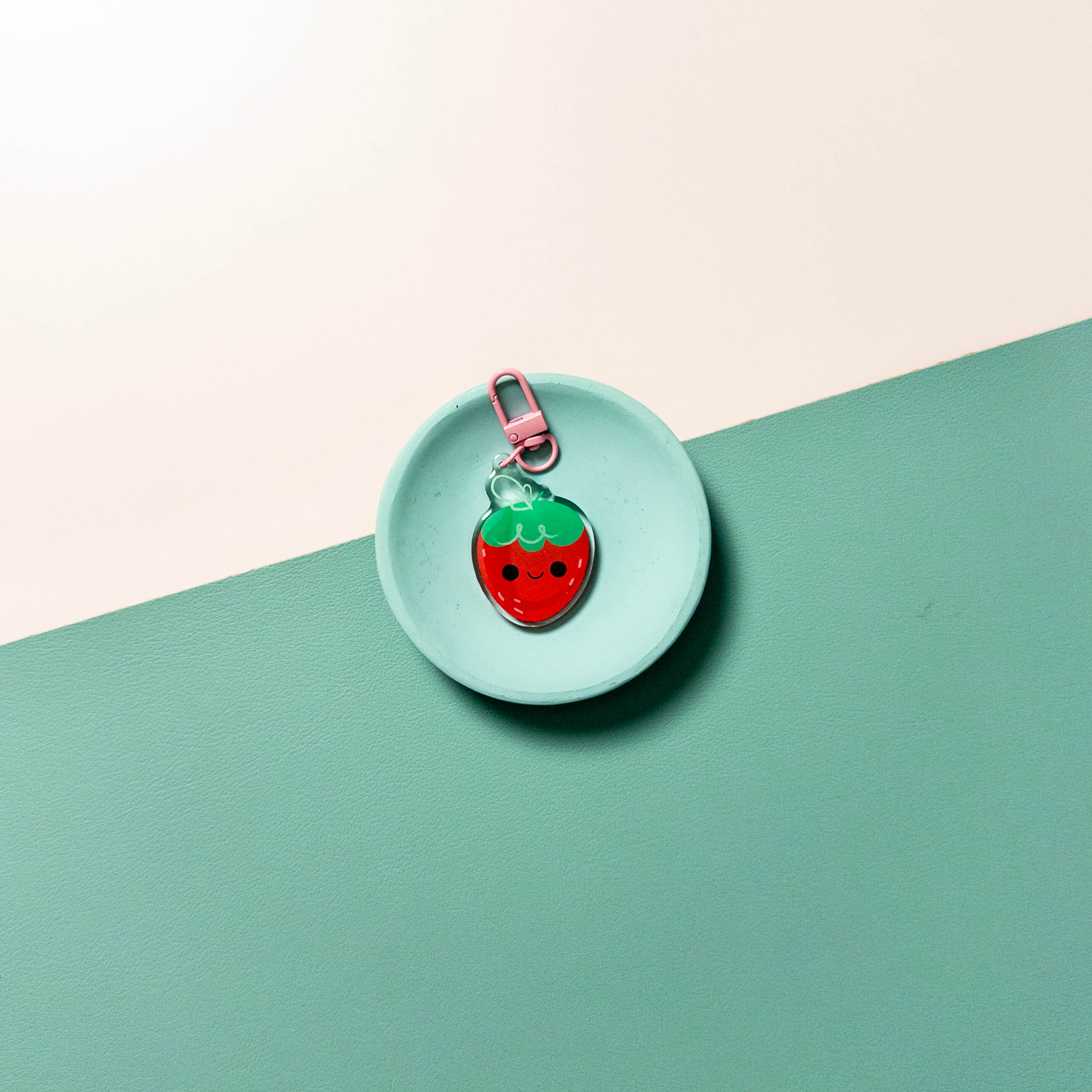 Strawberry-shaped keychain on a round turquoise tray with a light pink background