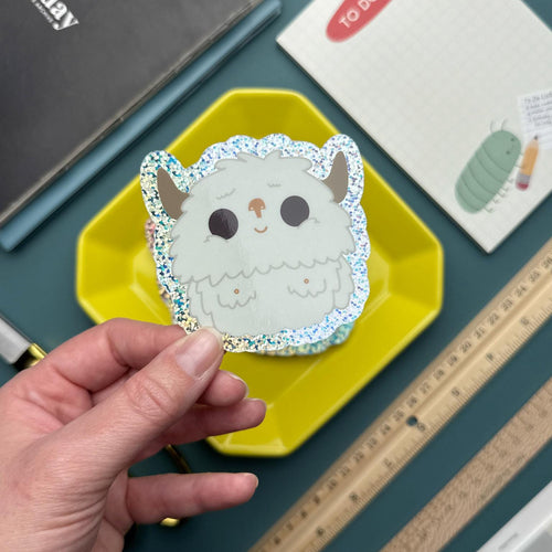 Hand holding a cute glittery yeti vinyl sticker, waterproof and scratch-resistant decal for laptops, water bottles, and journals, kawaii adventure design.