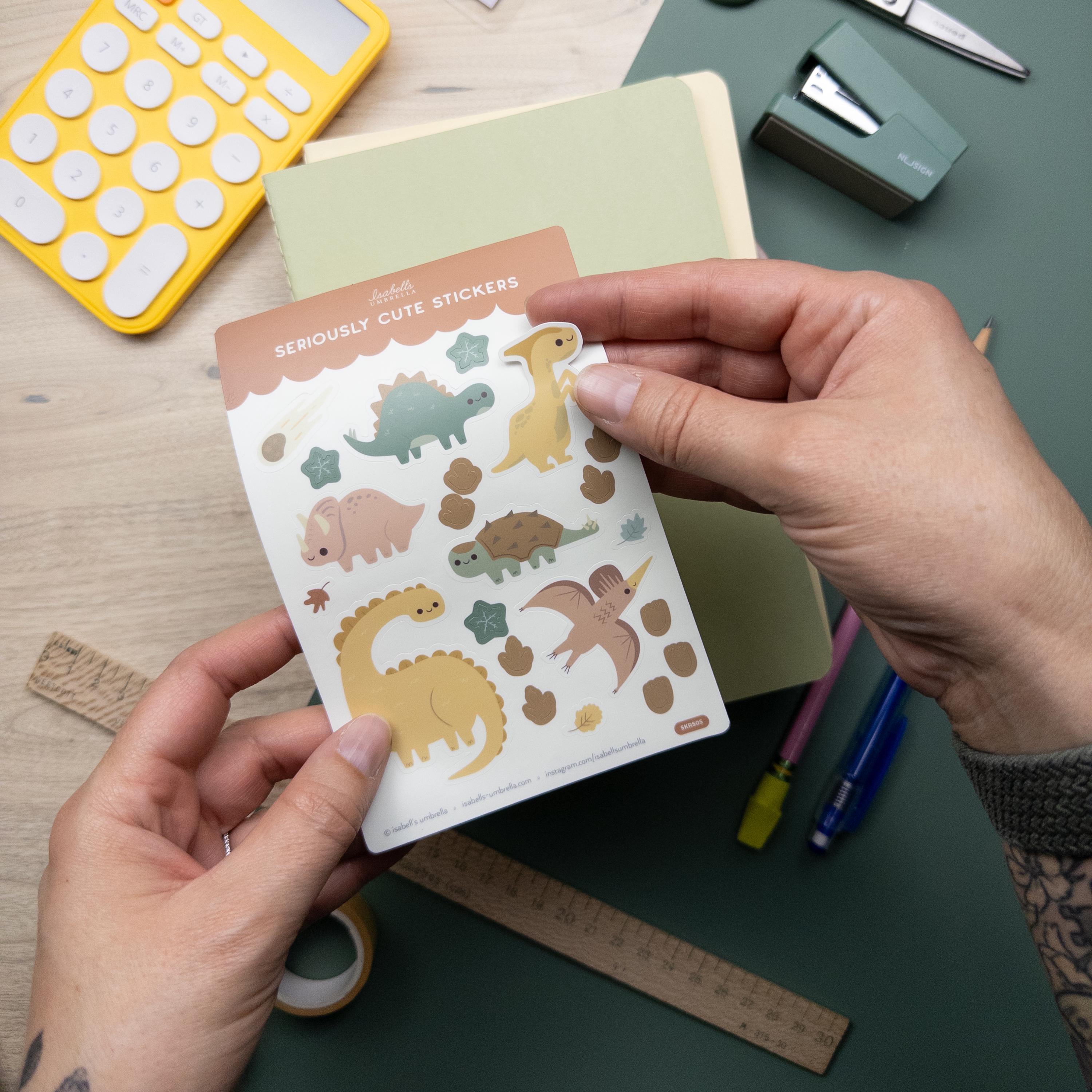hand peeling off a sticker of a yellow dinosaur on a sheet of stickers featuring six different dinosaurs.
