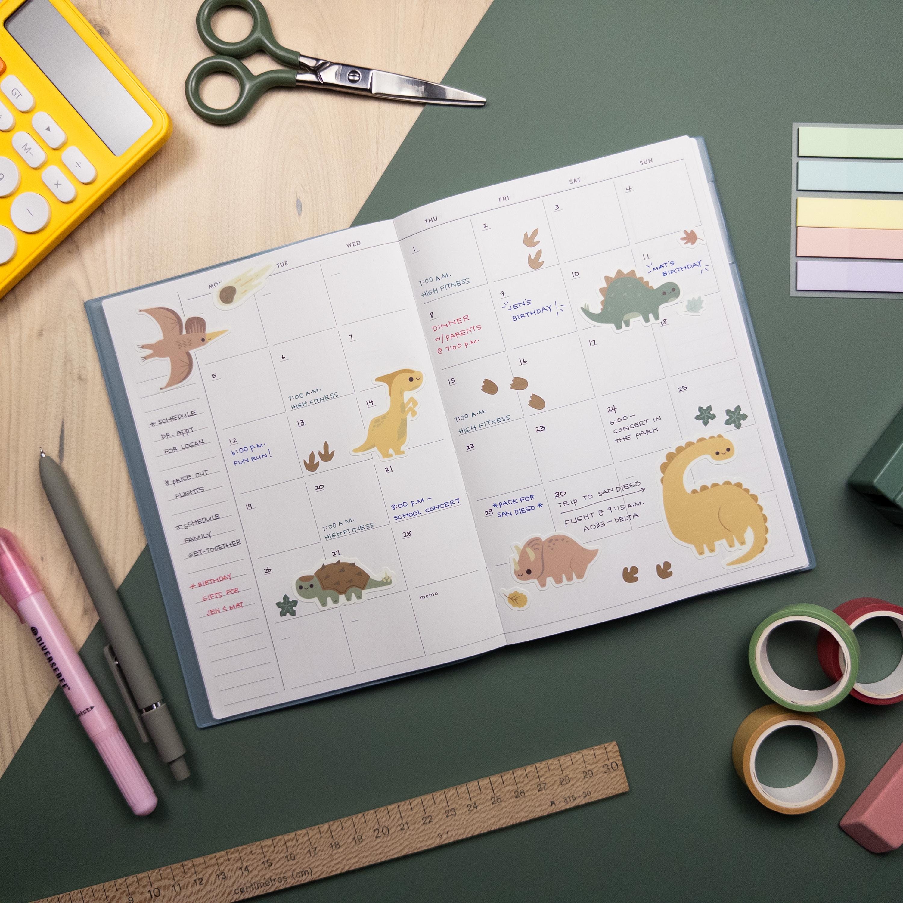 Top view of a calendar laying atop a desk. The calendar has been decorated with dinosaur themed stickers.