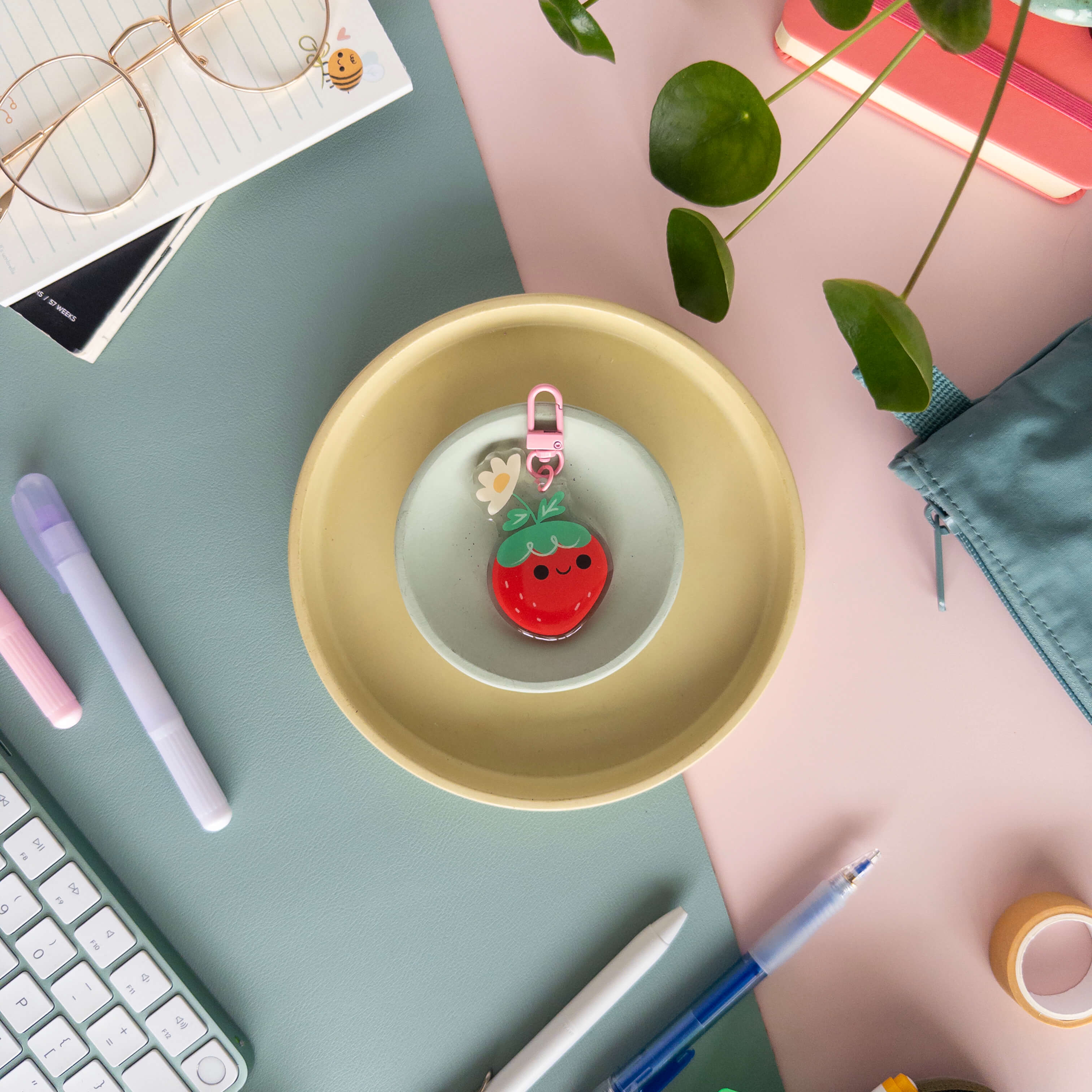 Yellow bowl with strawberry-themed keychain on a desk with stationery items