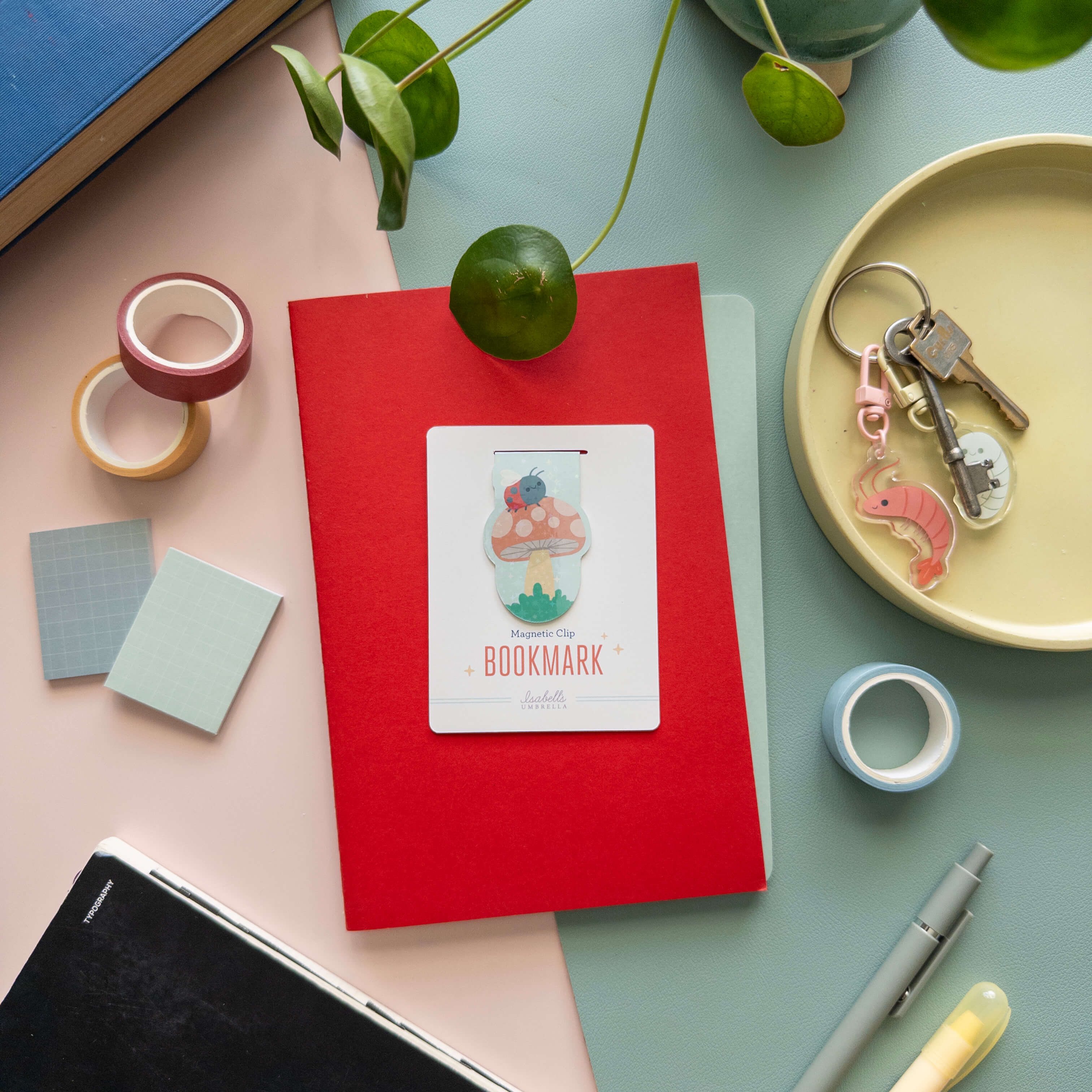 Red notebook with a magnetic bookmark of a mushroom with a ladybug, on a colorful surface with stationery items