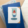 Magnetic bookmark featuring an illustrated gnome packaged and sitting on top of a stack of books.